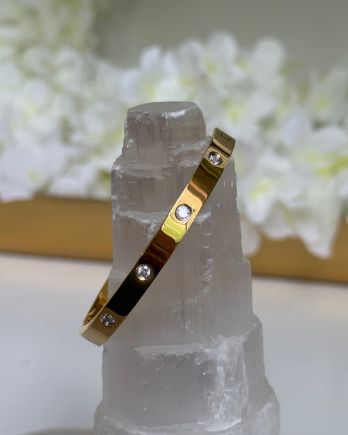 Gold bracelet with embedded stones on a crystal stand with a floral background