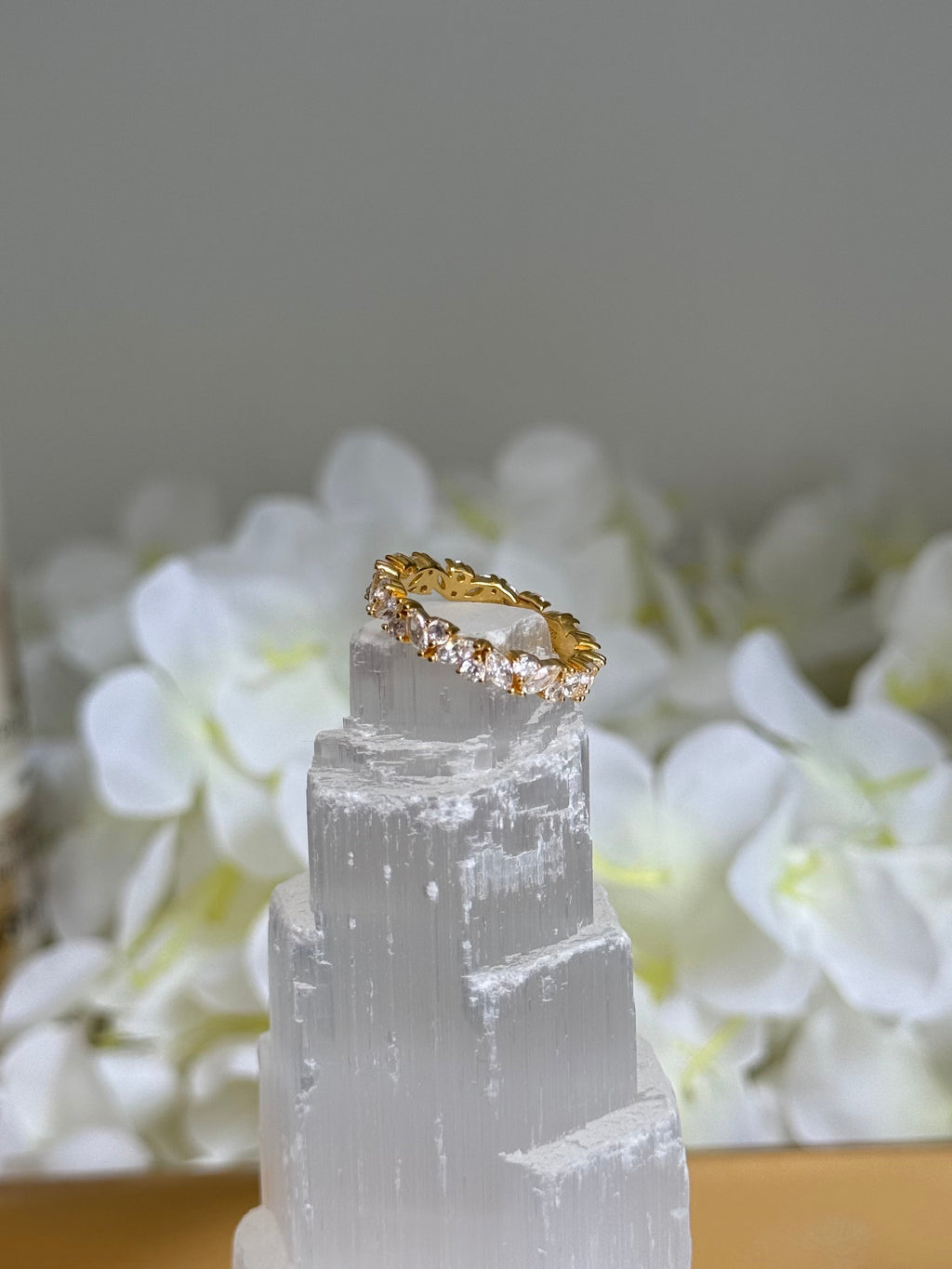 Gold ring on a clear crystal with white flowers in the background