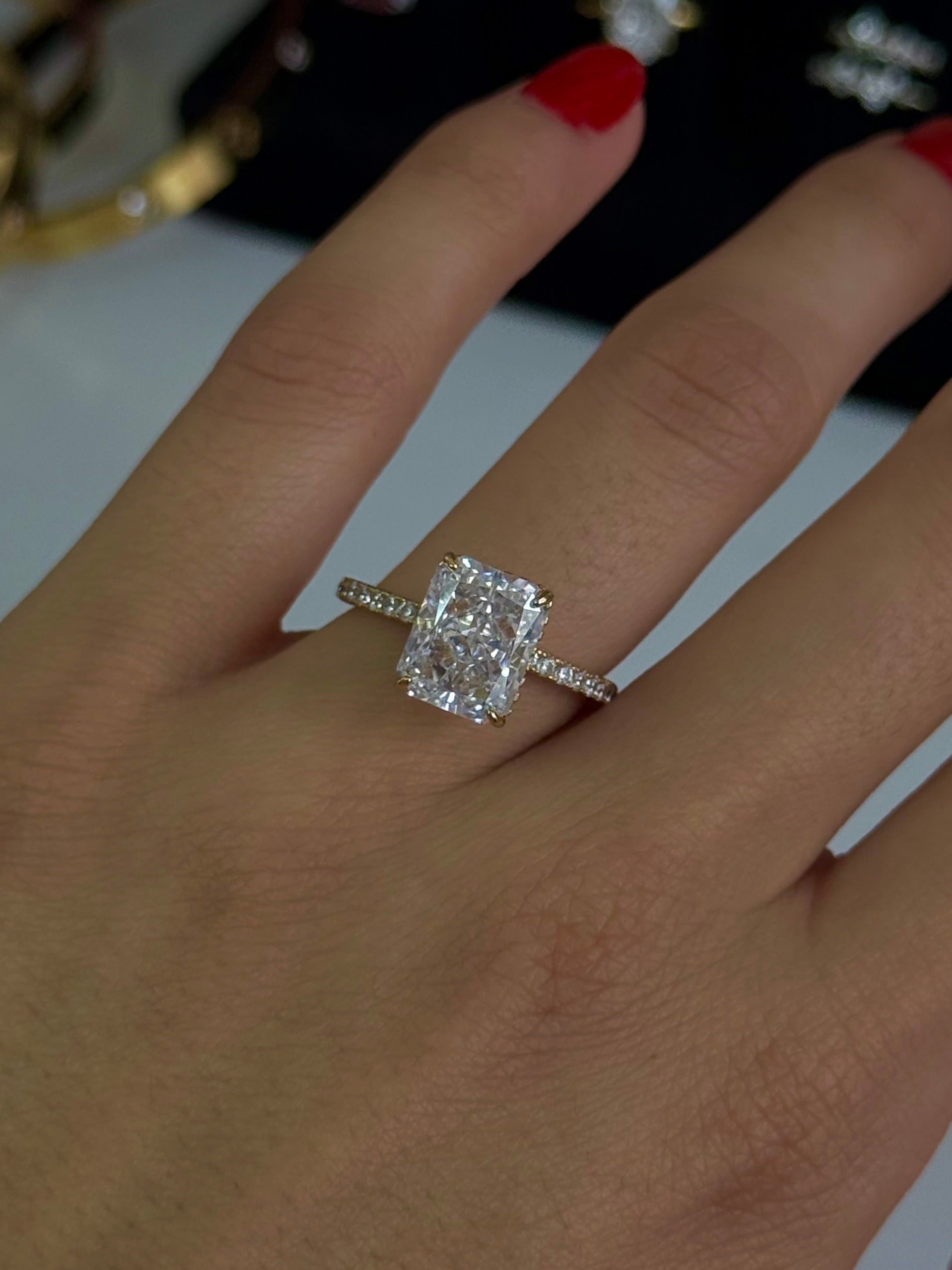 A close-up of a hand wearing a silver-toned ring with a large cushion-cut clear gemstone, with other jewelry and a black display box blurred in the background.