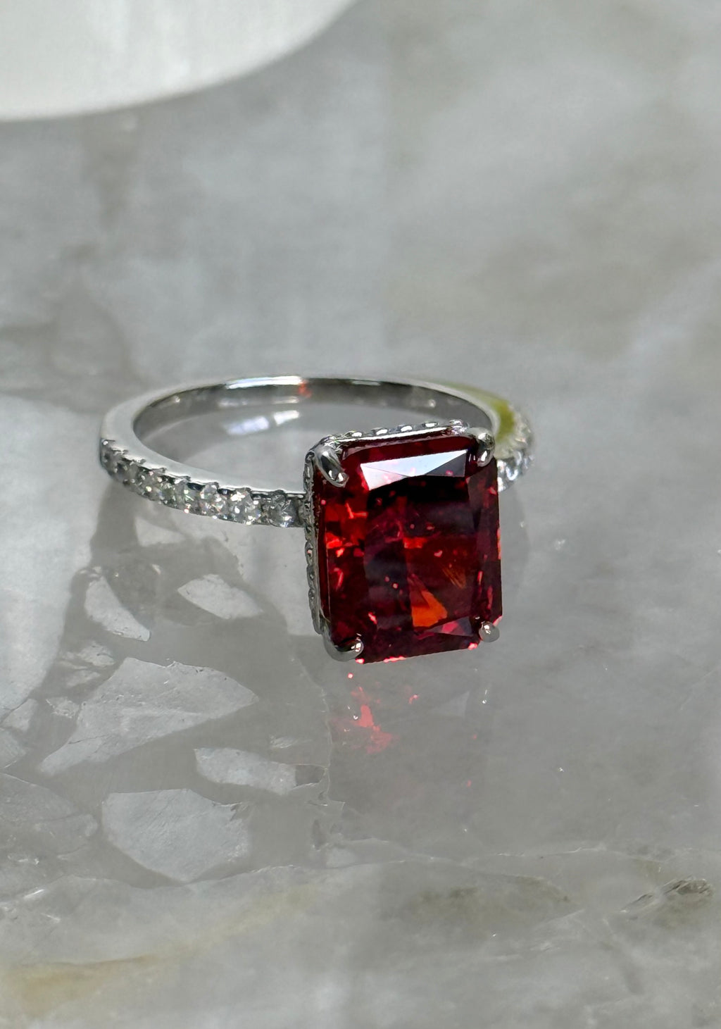 Silver ring with a red gemstone on a marble surface