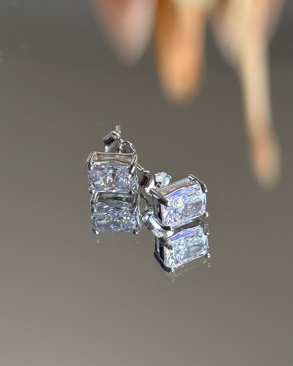 Diamond earrings on a reflective surface with a blurred background