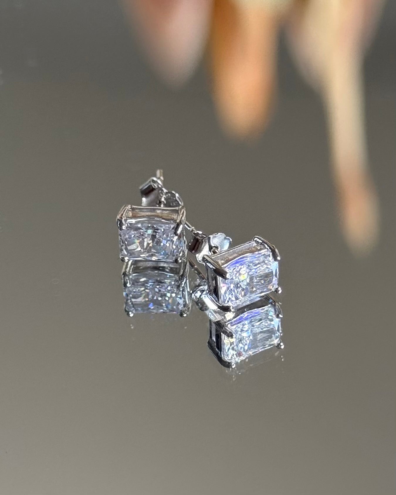 Diamond earrings on a reflective surface with a blurred background