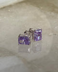 Pair of silver earrings with purple gemstones on a light gray surface