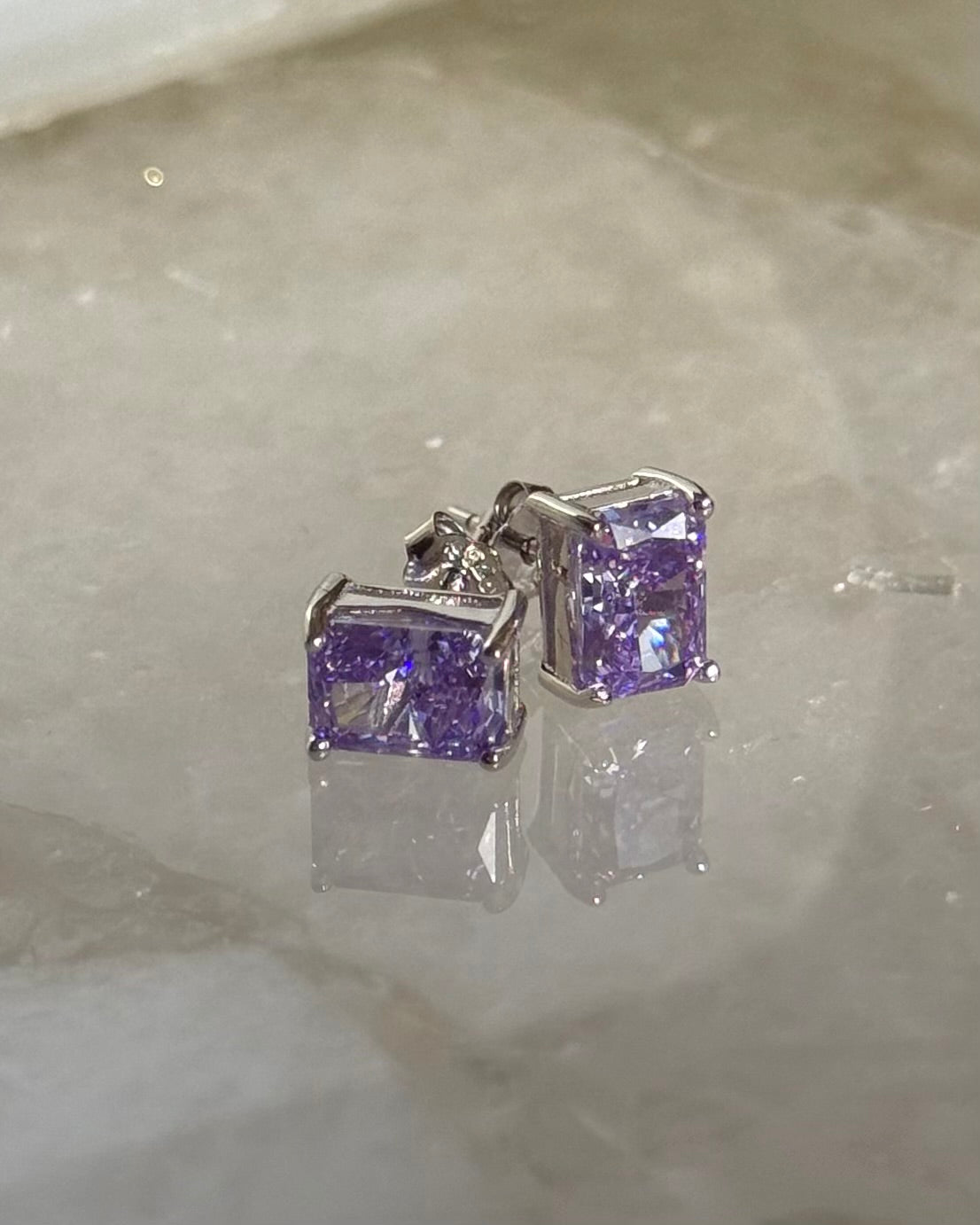 Pair of silver earrings with purple gemstones on a light gray surface