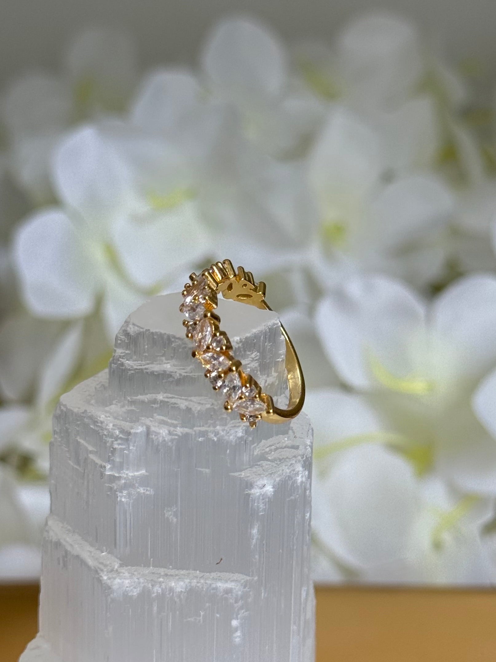 Gold ring with small diamonds on a white stone surface with white flowers in the background