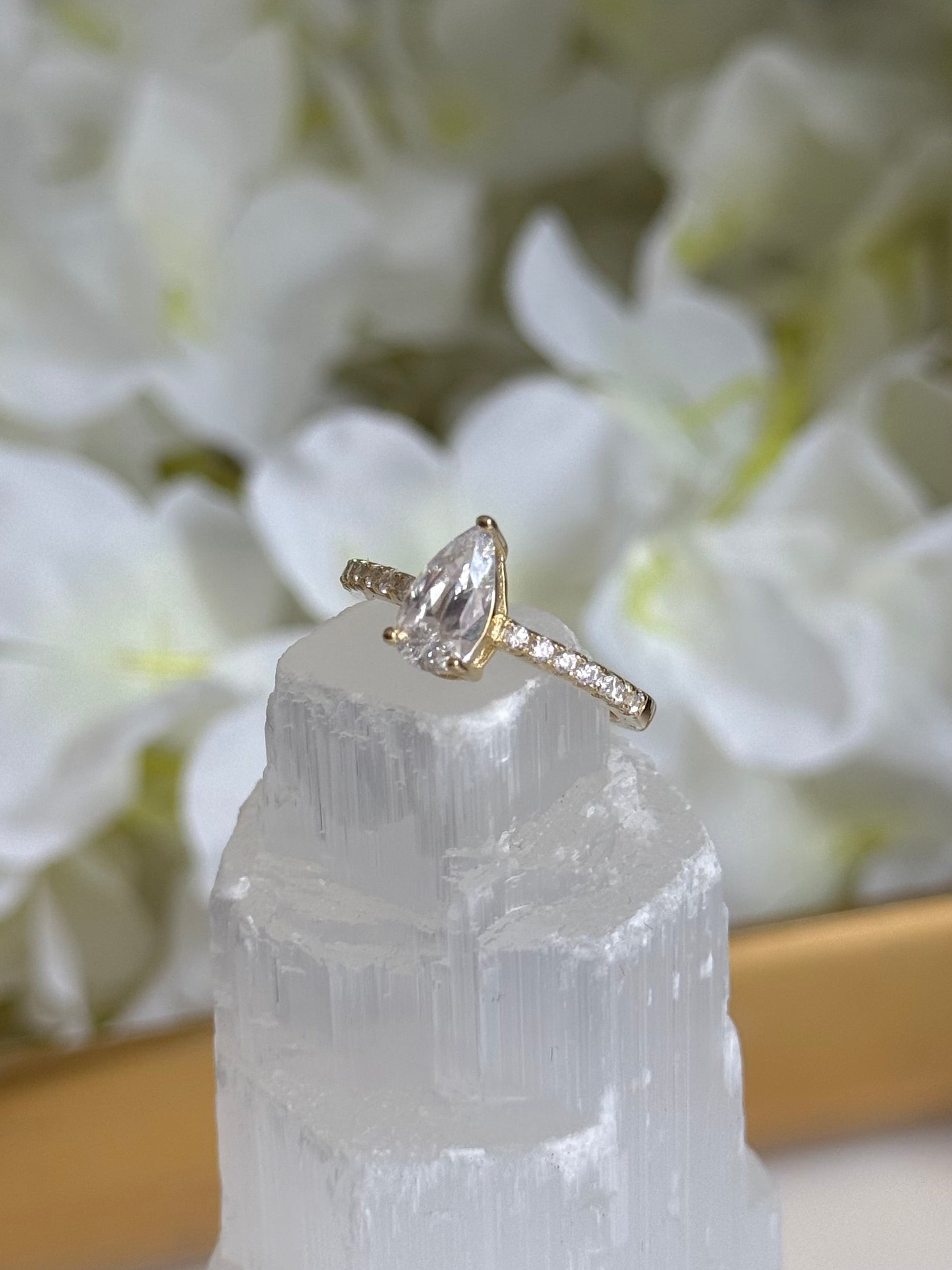 Gold ring with a clear gemstone held over white flowers and crystals
