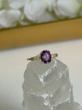 Gold ring with a purple gemstone on a clear crystal with white flowers in the background