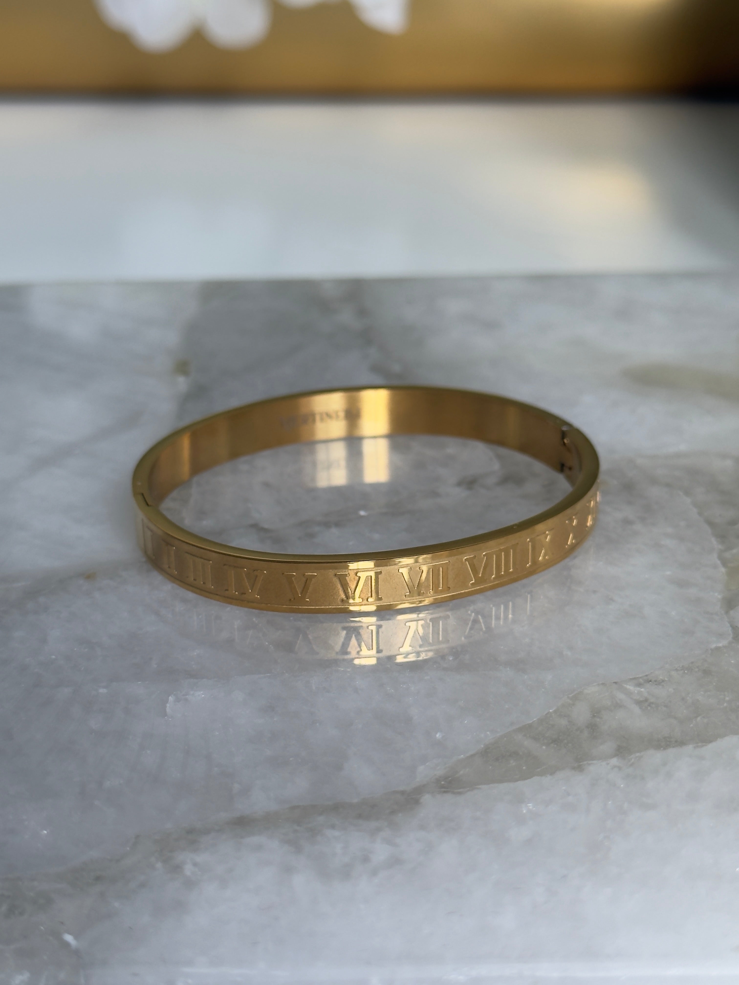 Gold bracelet with engraved design on a marble surface